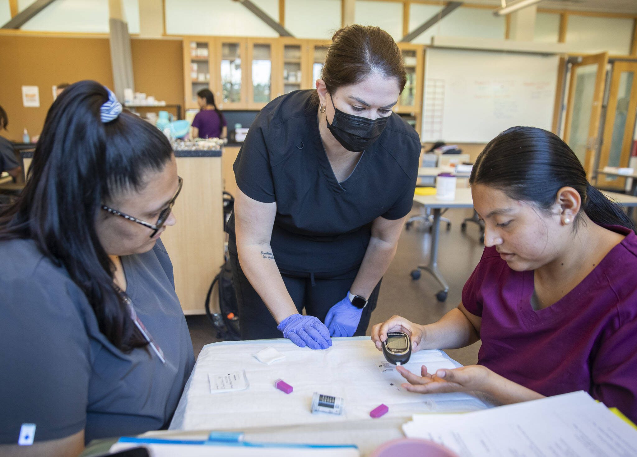 Abril Gonzalez, left, and instructor Amber Samaniego, center, watch as Aleyda Chuc tests her glucose levels on Wednesday, Aug. 7, 2024 in Everett, Washington. (Olivia Vanni / The Herald)