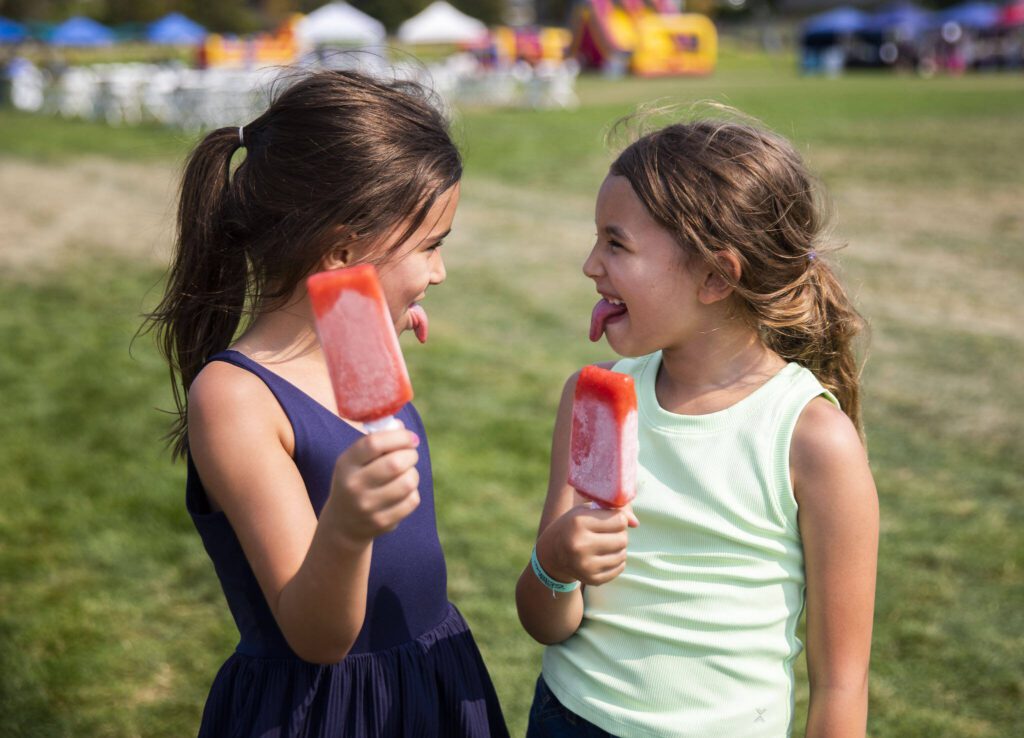 Olivia Moreno, 7, left, and Vida Coppola, 7, make faces at each other while eating their Seattle Pops at Taste Edmonds on Friday in Edmonds. (Olivia Vanni / The Herald)

