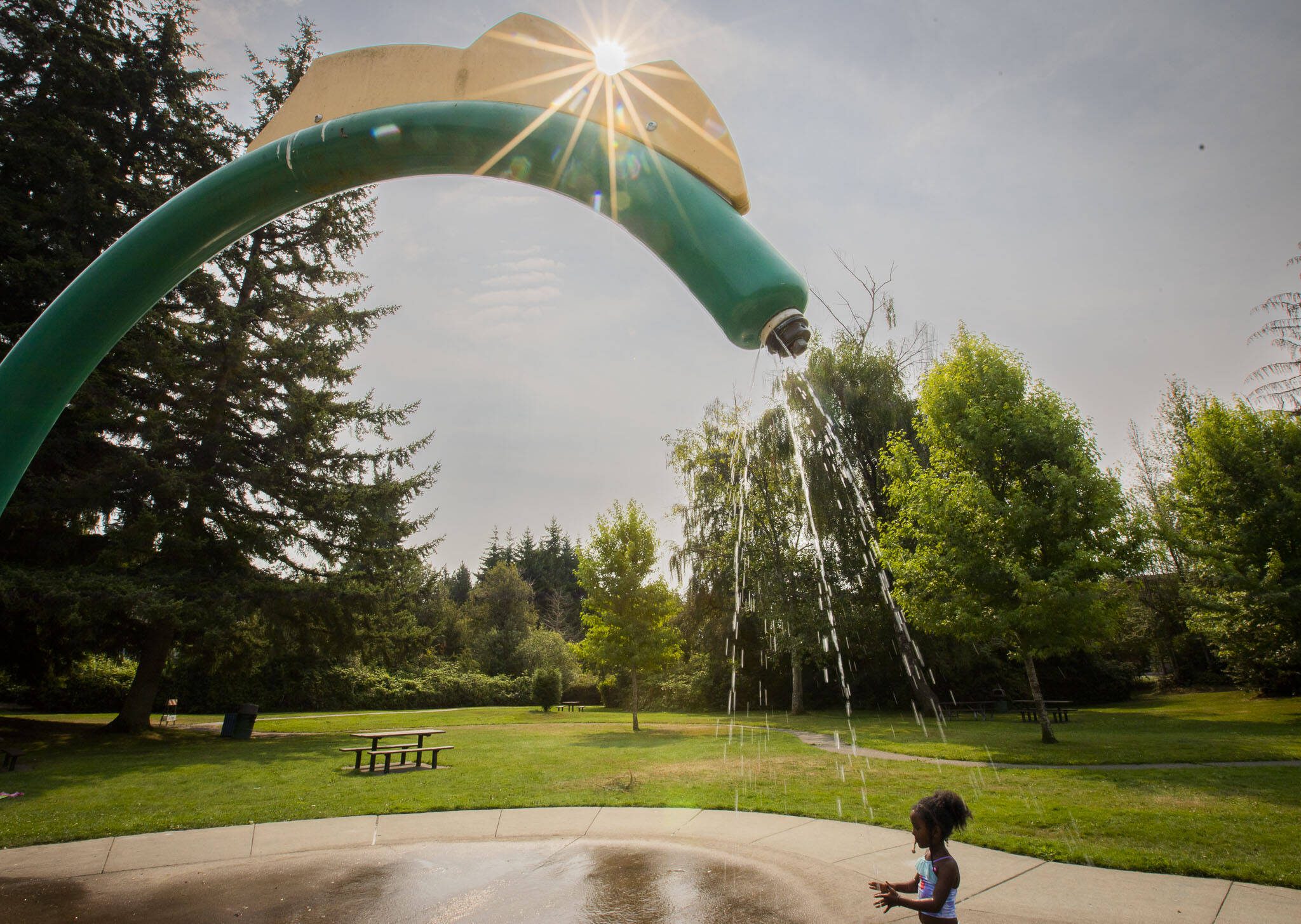 Bethayna Gebremariam, 6, is sprayed with water while the sun casts orange-tinged light across North Lynnwood Park on Friday, Aug. 9, 2024 in Lynnwood, Washington. (Olivia Vanni / The Herald)
