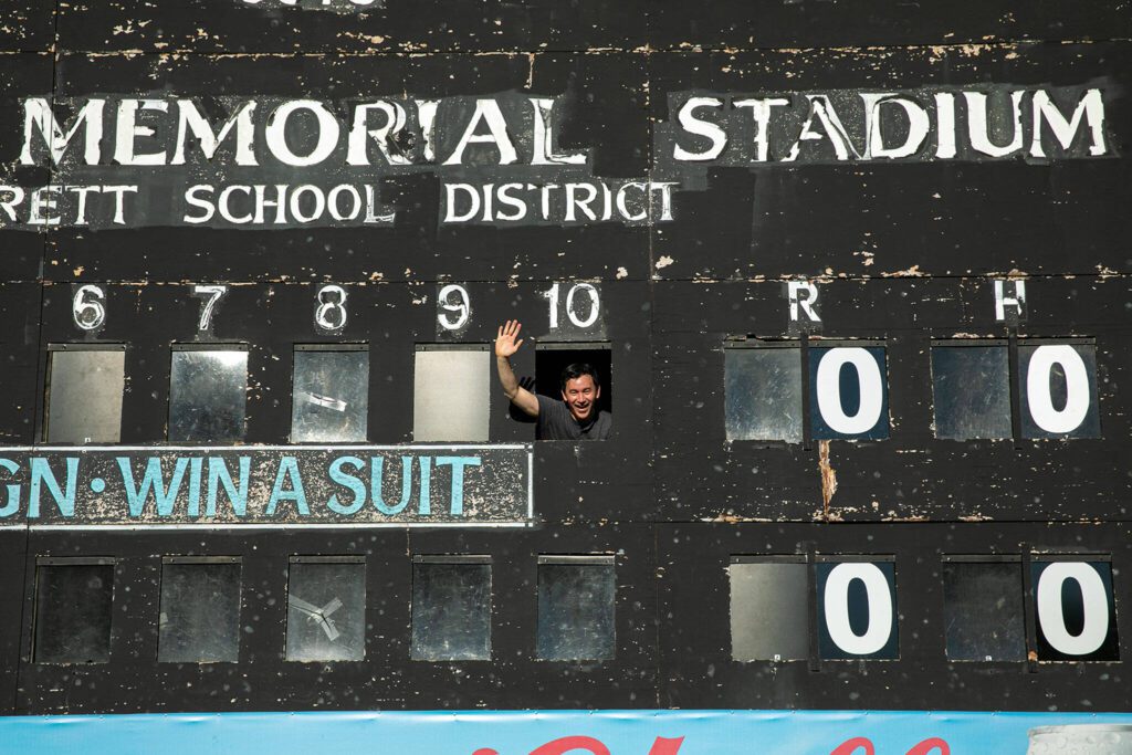 Herald sports reporter Nick Patterson waves from an opening in the Funko Field manual scoreboard on July 23, 2022, before an AquaSox game in Everett.
