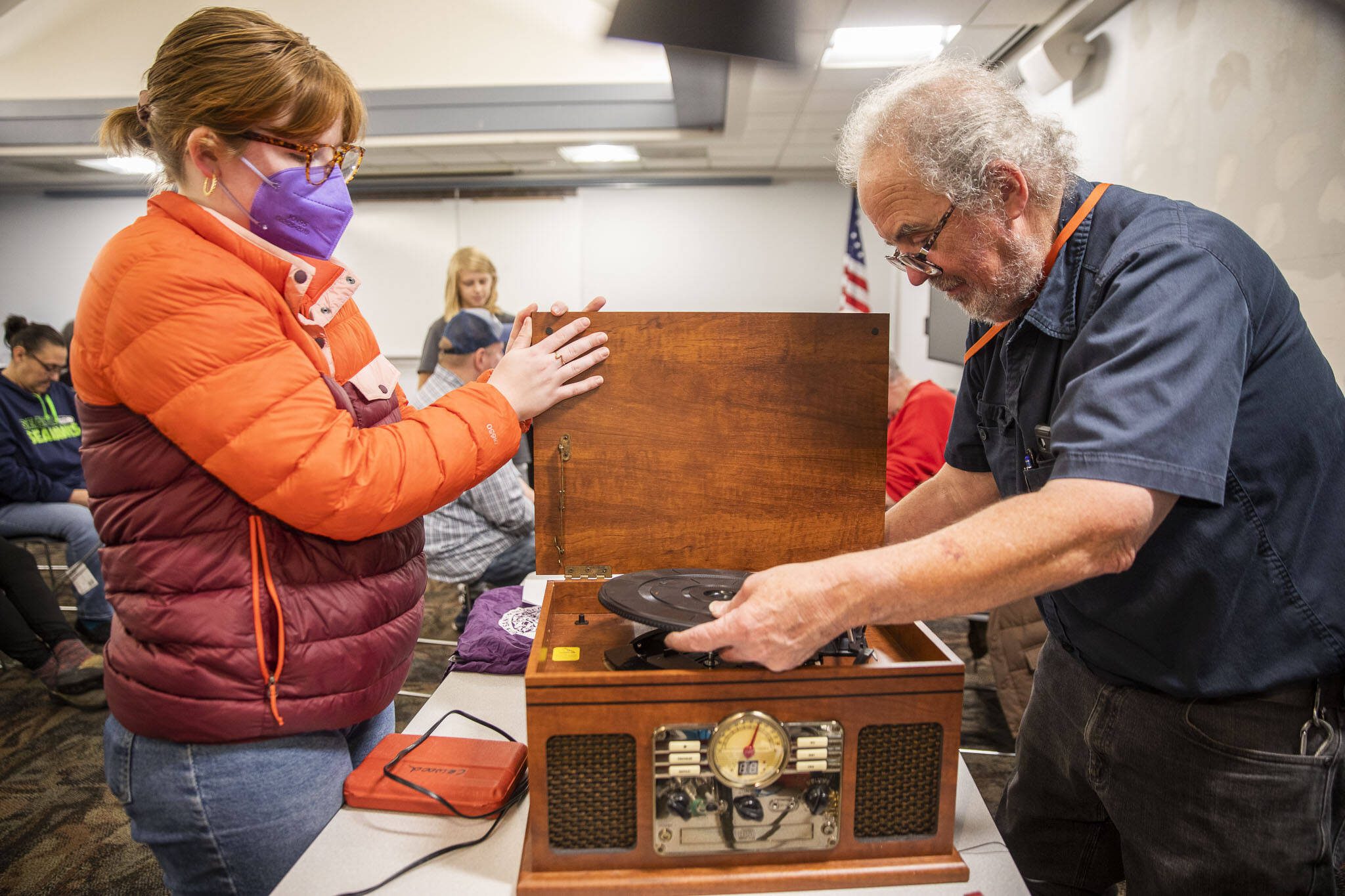 Clark Wood, right, starts repairs on a record player brought in to the Repair Cafe in 2023 in Mountlake Terrace. (Olivia Vanni / The Herald)