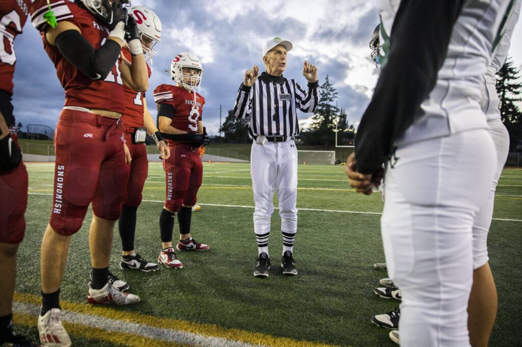 Tom Freal, who is in his 50th year of officiating, explains the coin toss to the captains of the Snohomish and Mount Vernon football teams before the start of the game on Friday, Oct. 4, 2024 in Snohomish, Washington. (Olivia Vanni / The Herald)
