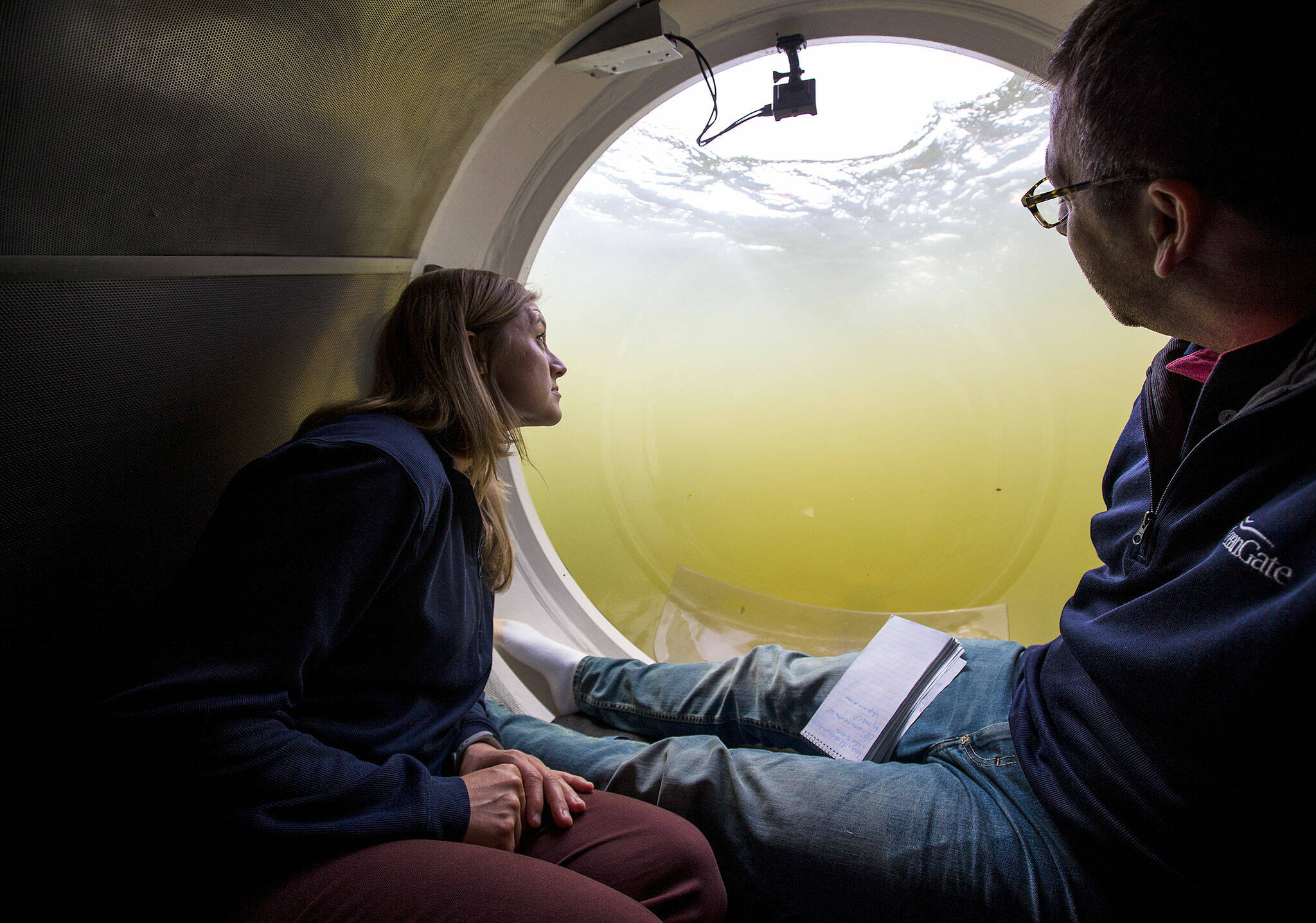Bonnie Carl, left, and Josh Dean look out the dome as the OceanGate submarine Cyclops1 submerges in the Port of Everett Marina in 2017 in Everett. (Andy Bronson / The Herald)