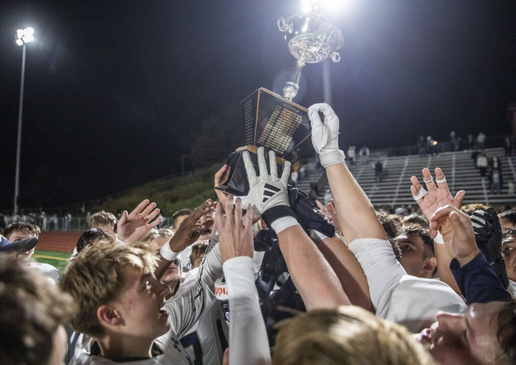 Arlington players lift the Stilly Cup in the air after beating Stanwood on Friday, Oct. 11, 2024 in Stanwood, Washington. (Olivia Vanni / The Herald)
