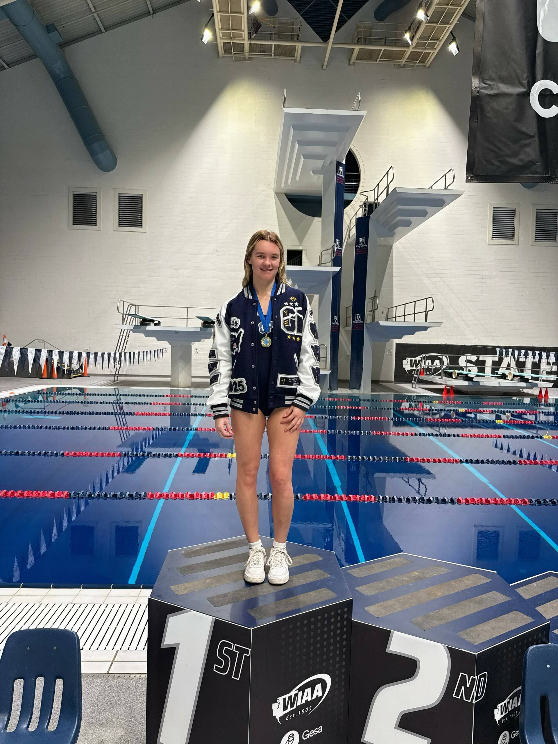 Glacier Peak High School diver Addison Farman stands on the championship platform after winning her second straight Class 4A 1-meter diving title at the King Country Aquatics Center on Thursday, Nov. 14, 2024. (Photo courtesy of Jamie Farman)
