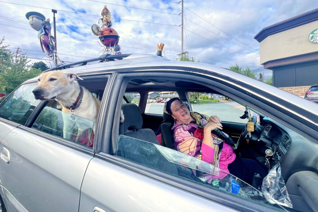 A woman, who identified herself as “Blue,” poses for a photo while sitting in a parking lot at a Safeway in Everett in July 2024. (Andrea Brown / For the Herald)
