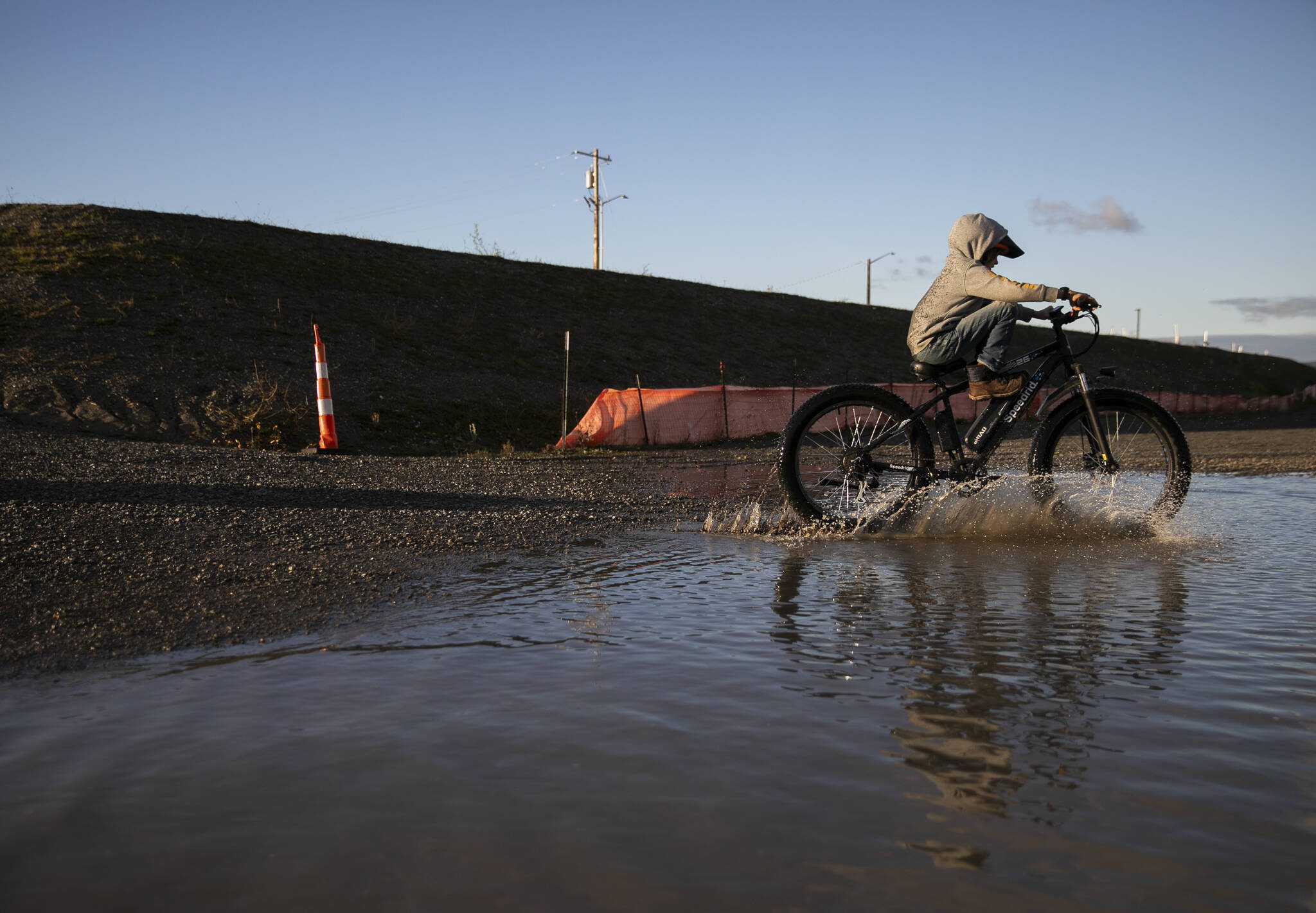 The Nosov family rides their bikes through a large puddle that formed next to the large piles of fill dirt at the Port of Everett on Monday, Dec. 9, 2024 in Everett, Washington. (Olivia Vanni / The Herald)