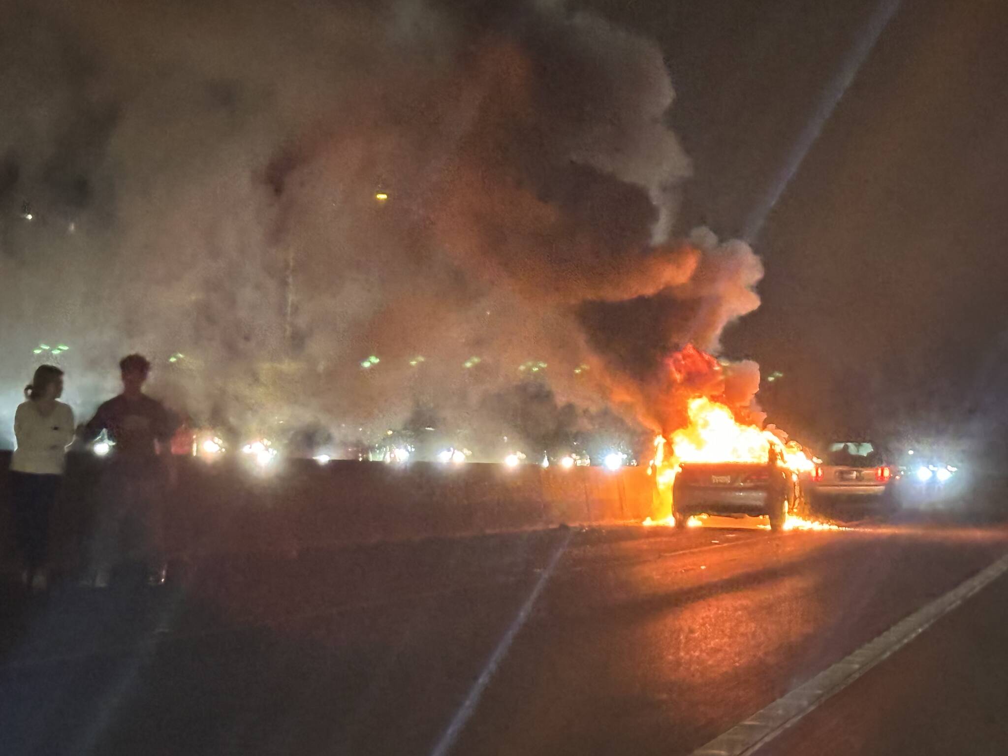 Two people stand on the highway as a car burns in the southbound lanes of Interstate 5 on Monday, Dec. 30 near Mountlake Terrace, Washington. (Eliza Aronson / The Herald)