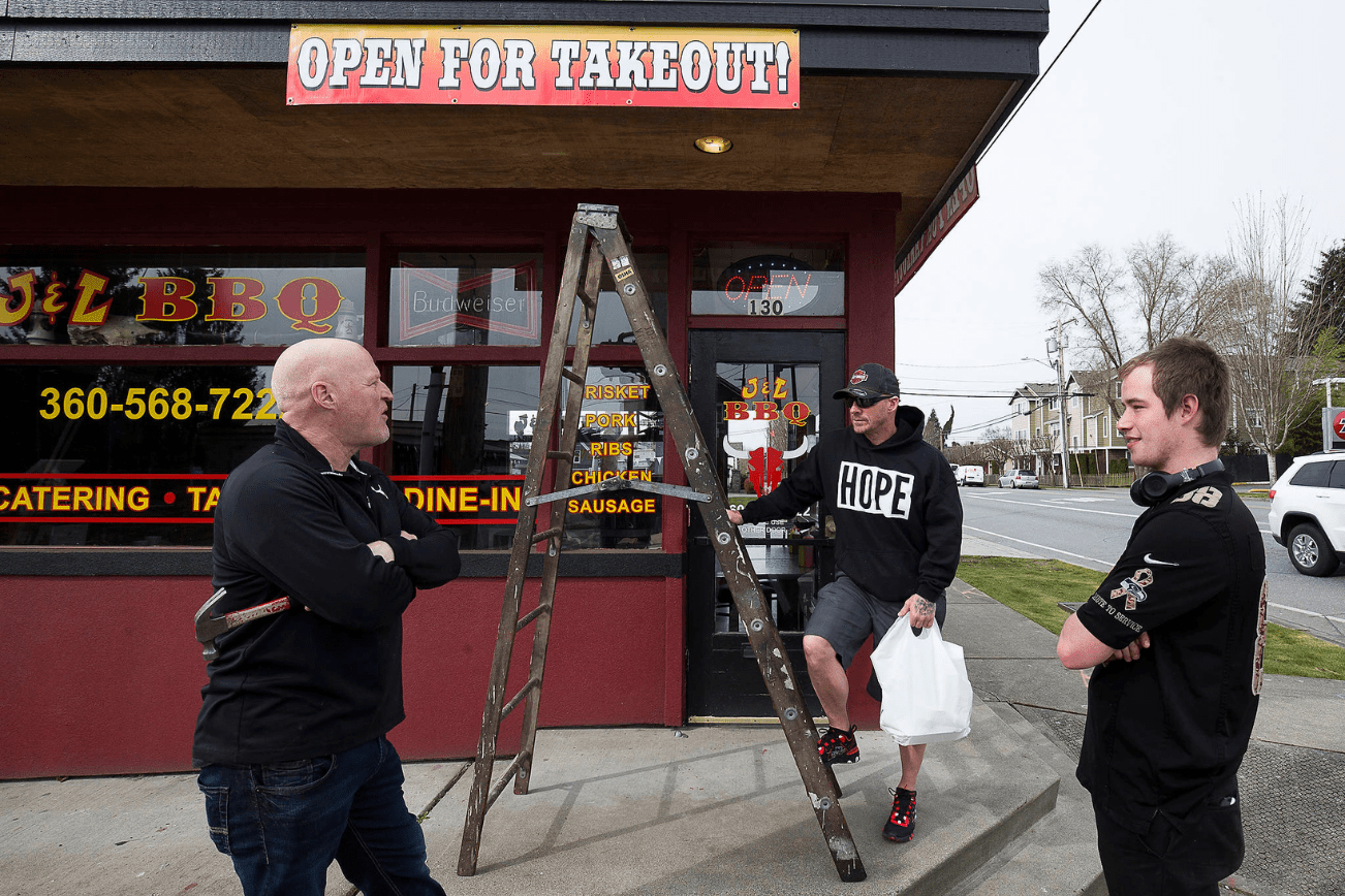 At J&L BBQ in Snohomish, owner Joel Sexton (left) talks with customer Tony Cecsarini and Austin Eisenhuth (right) after hanging banners announcing the restaurant’s ability to accept takeout orders. (Andy Bronson / The Herald)