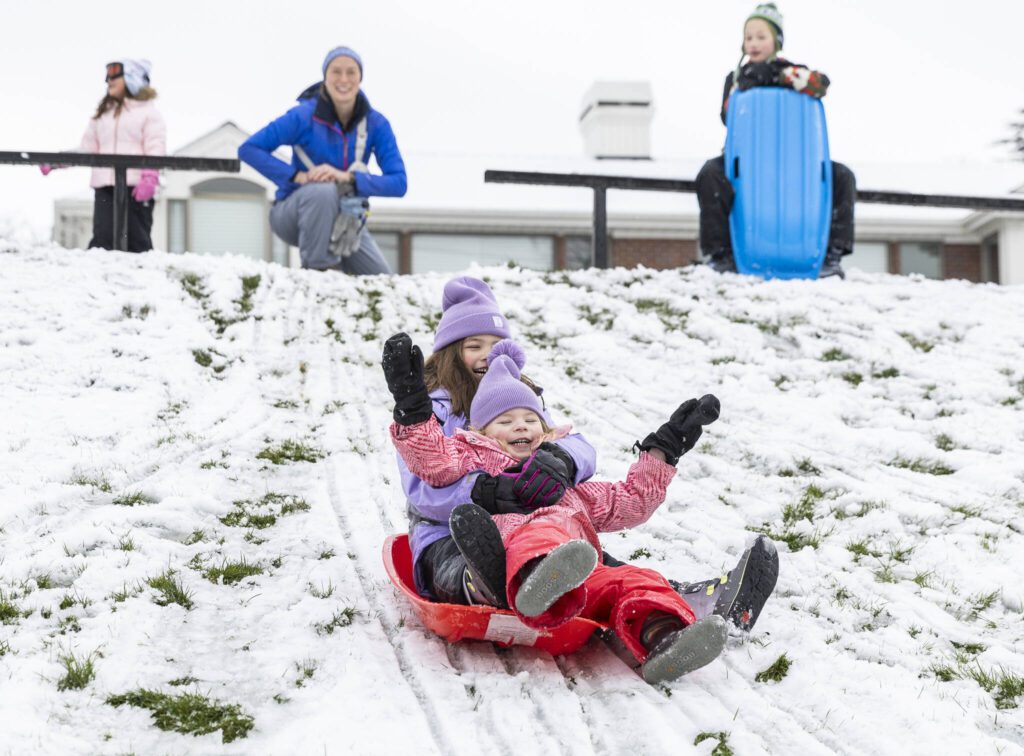 Riley Boyd, 6, left, and sisters Vivienne Boyd, 3, ride a sled together down a hill at Anderson Center Field on Thursday, Feb. 6, 2025 in Edmonds, Washington. (Olivia Vanni / The Herald)
