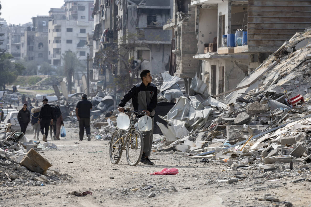 A young man carries water past the destroyed buildings of a neighborhood in the Gaza Strip, Feb. 2, 2025. President Donald Trump’s proposal to “own” the Gaza Strip and transfer its population elsewhere has stirred condemnation and sarcasm, but it addresses a real and serious challenge: the future of Gaza as a secure, peaceful, even prosperous place. (Saher Alghorra/The New York Times)
