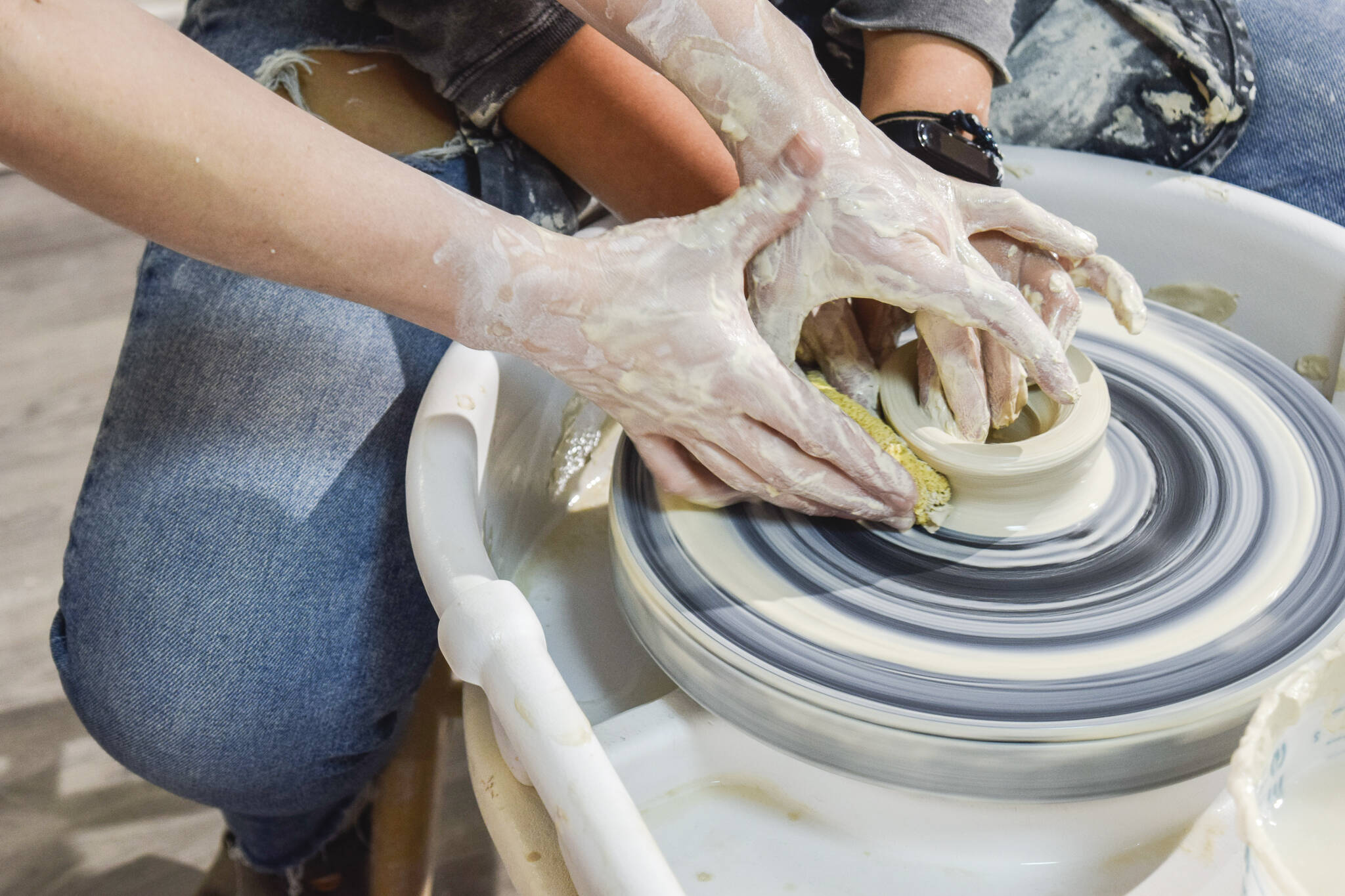 Whidbey Clay Center instructor Jordan Jones helps a student avoid a wobble disaster as she learns the first steps to throwing clay during her class. (Patricia Guthrie / Special to The Herald)