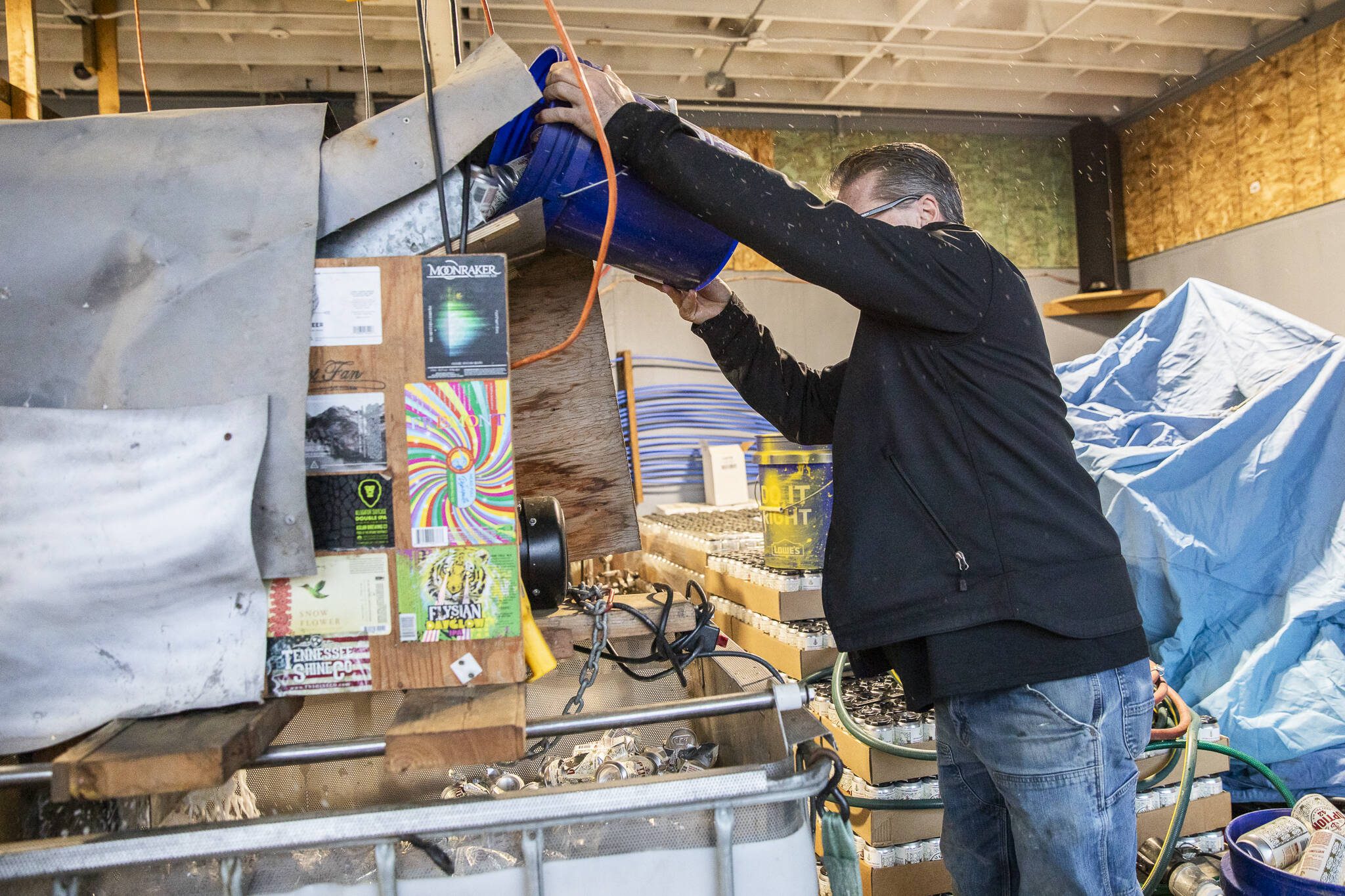 Robert Thompson pours a bucket of expired beer cans into his beer crusher. (Olivia Vanni / The Herald)