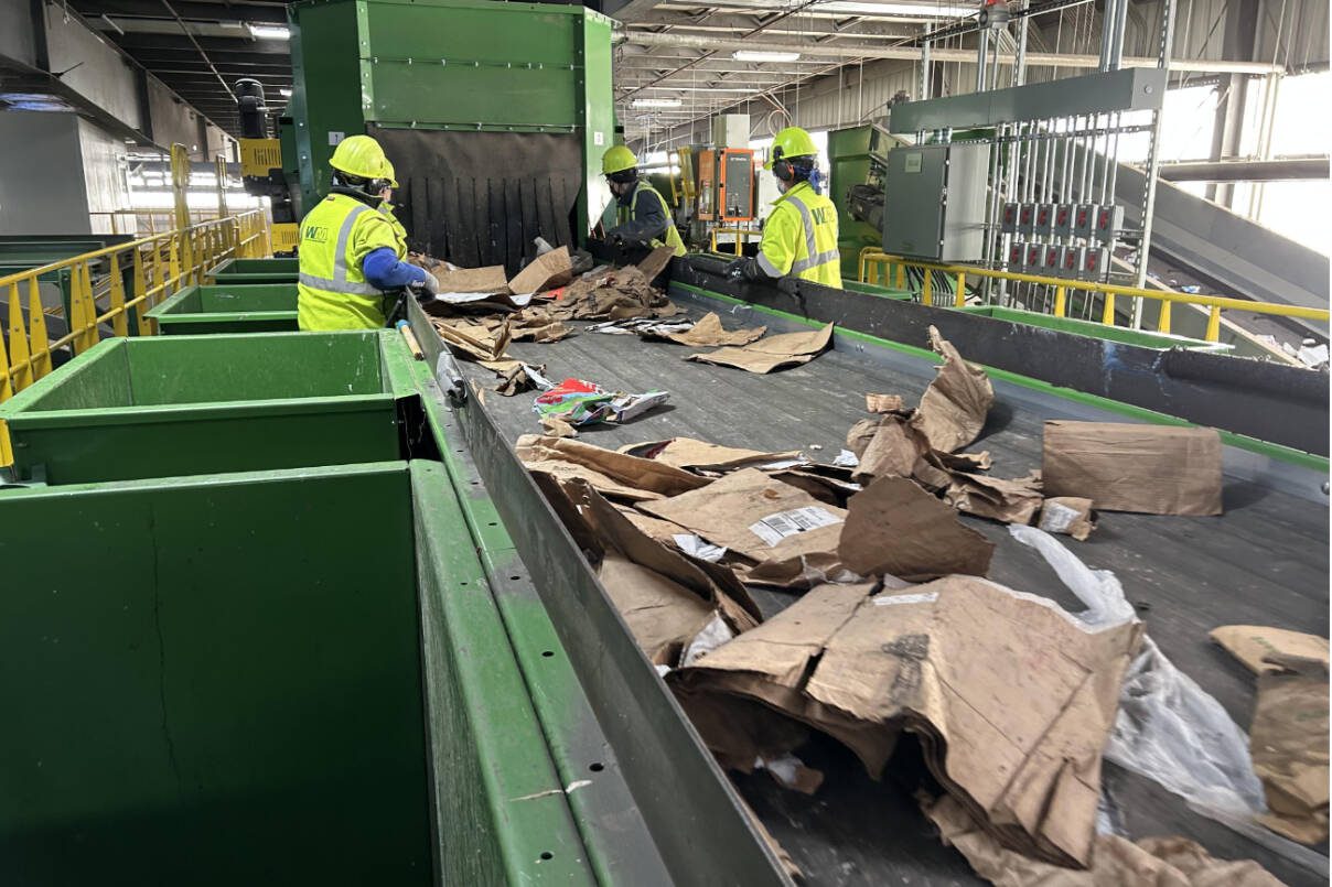 Workers at Waste Management’s Cascade Recycling Center in Woodinville remove large unrecyclable materials, like plastic sheeting, from a conveyor belt. Optical scanners and other equipment sort most of the material processed at the center. (The Herald file photo)