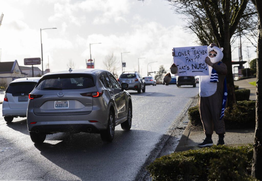 Scott Haddock holds a sign protesting teacher pay cuts during a Edmonds College faculty union rally as part of a national day of action outside of the Lynnwood Event Center on Tuesday, March 4, 2025 in Lynnwood, Washington. (Olivia Vanni / The Herald)
