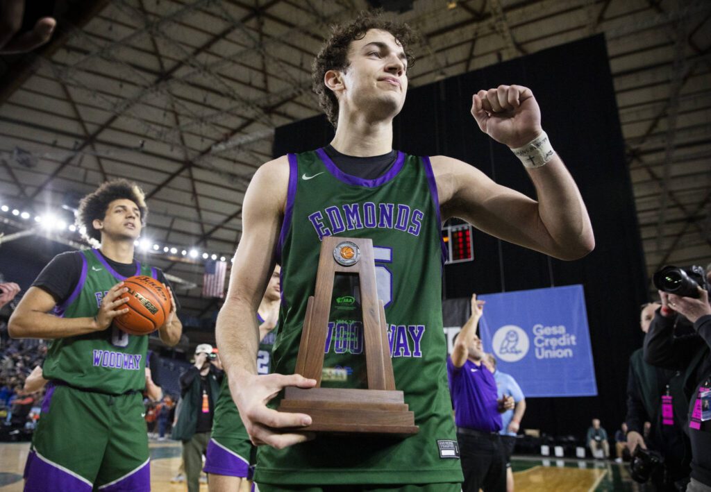 Edmonds-Woodway’s Cam Hiatt brings th 3A boys second place trophy over the the fan section and raises his fist in thanks to fans on Saturday, March 8, 2025 in Tacoma, Washington. (Olivia Vanni / The Herald)
