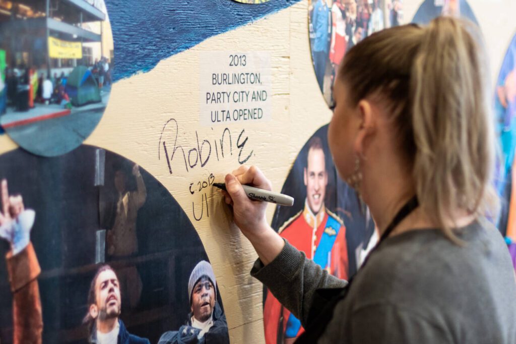 Ulta Beauty employee Robin Earle signs the timeline mural on Thursday in the food court of the Everett Mall, Thursday, March 20, 2025, in Everett, Washington. (Aaron Kennedy / The Herald)
