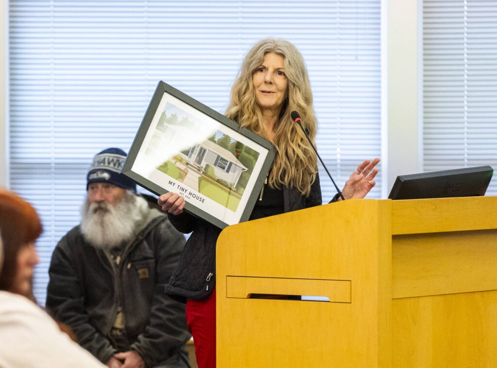 Christine Hurley holds a picture of her home as she speaks against a proposed Medical District Expansion near Swedish Edmonds at the city council meeting on Monday, April 21, 2025 in Edmonds, Washington. (Olivia Vanni / The Herald)
