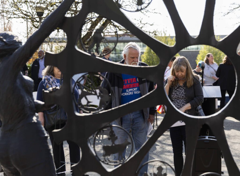 People pause to read names etched in brick at the base of a memorial statue during a ceremony on Worker’s Memorial Day on Wednesday, April 23, 2025 in Everett, Washington. (Olivia Vanni / The Herald)
