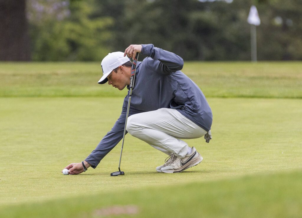 Snohomish’s Tully VanAssche places his ball on the green to putt during the 3A District 1 Boys Golf Championship at Legion Memorial Golf Course on Tuesday, May 13, 2025 in Everett, Washington. (Olivia Vanni / The Herald)
