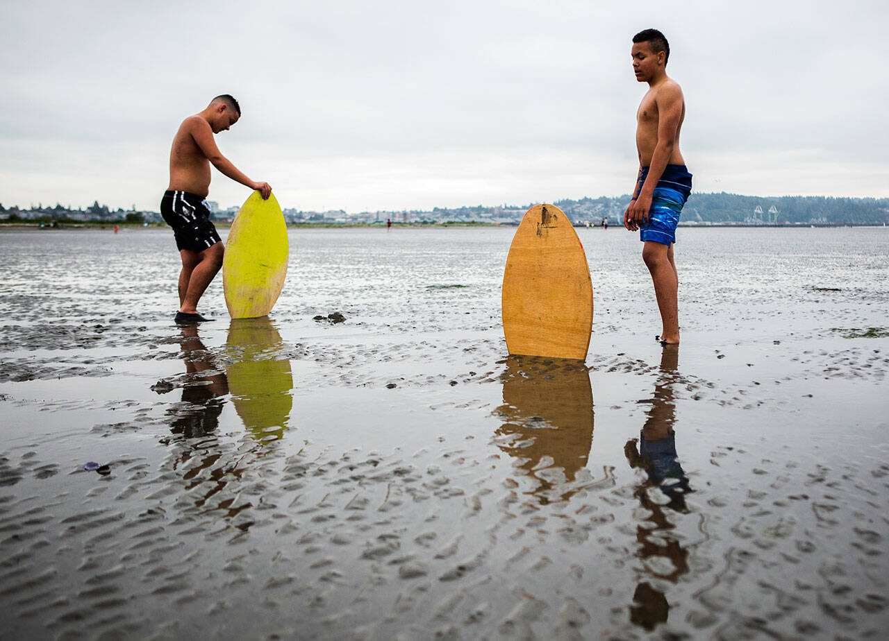 Ellis Johnson, 16, left, and brother Garrett Johnson, 13, take a breather after trying to find enough water to skim board on without sinking into the sand during opening day of Jetty Island on Friday, July 5, 2019 in Everett, Wash. (Olivia Vanni / The Herald)