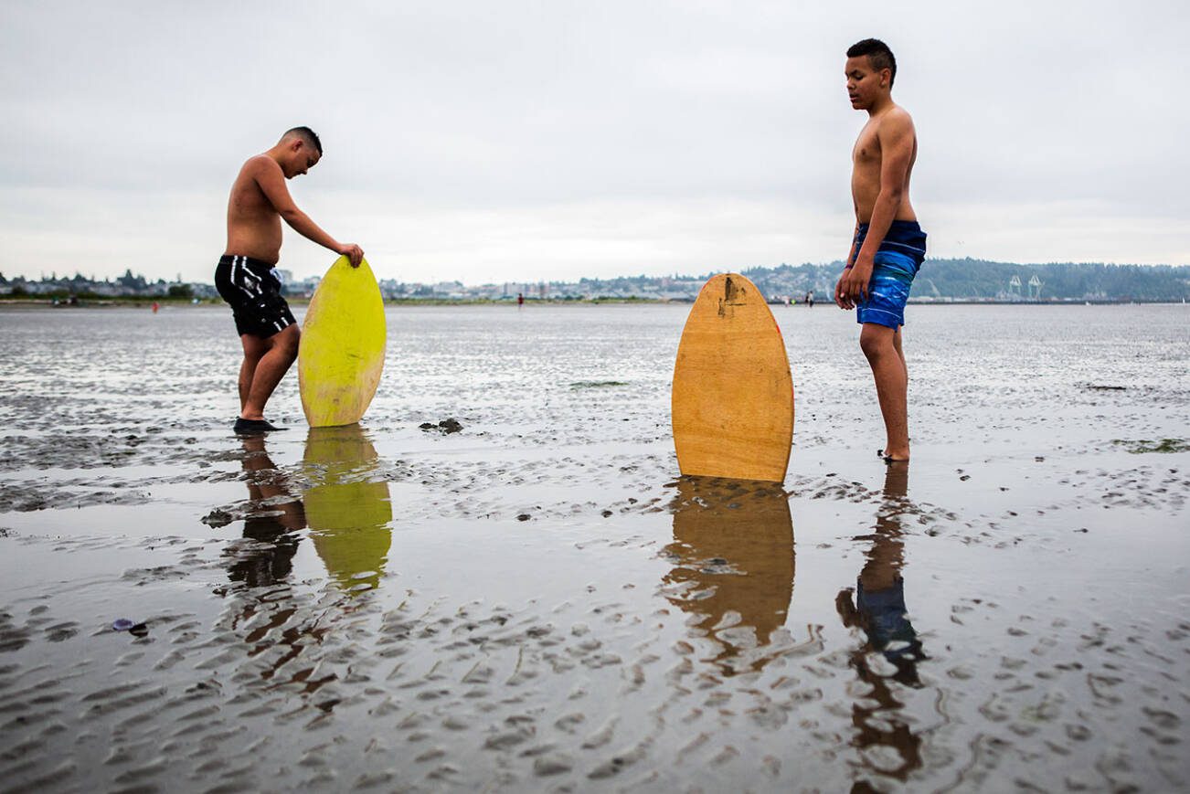 Ellis Johnson, 16, left, and brother Garrett Johnson, 13, take a breather after trying to find enough water to skim board on without sinking into the sand during opening day of Jetty Island on Friday, July 5, 2019 in Everett, Wash. (Olivia Vanni / The Herald)