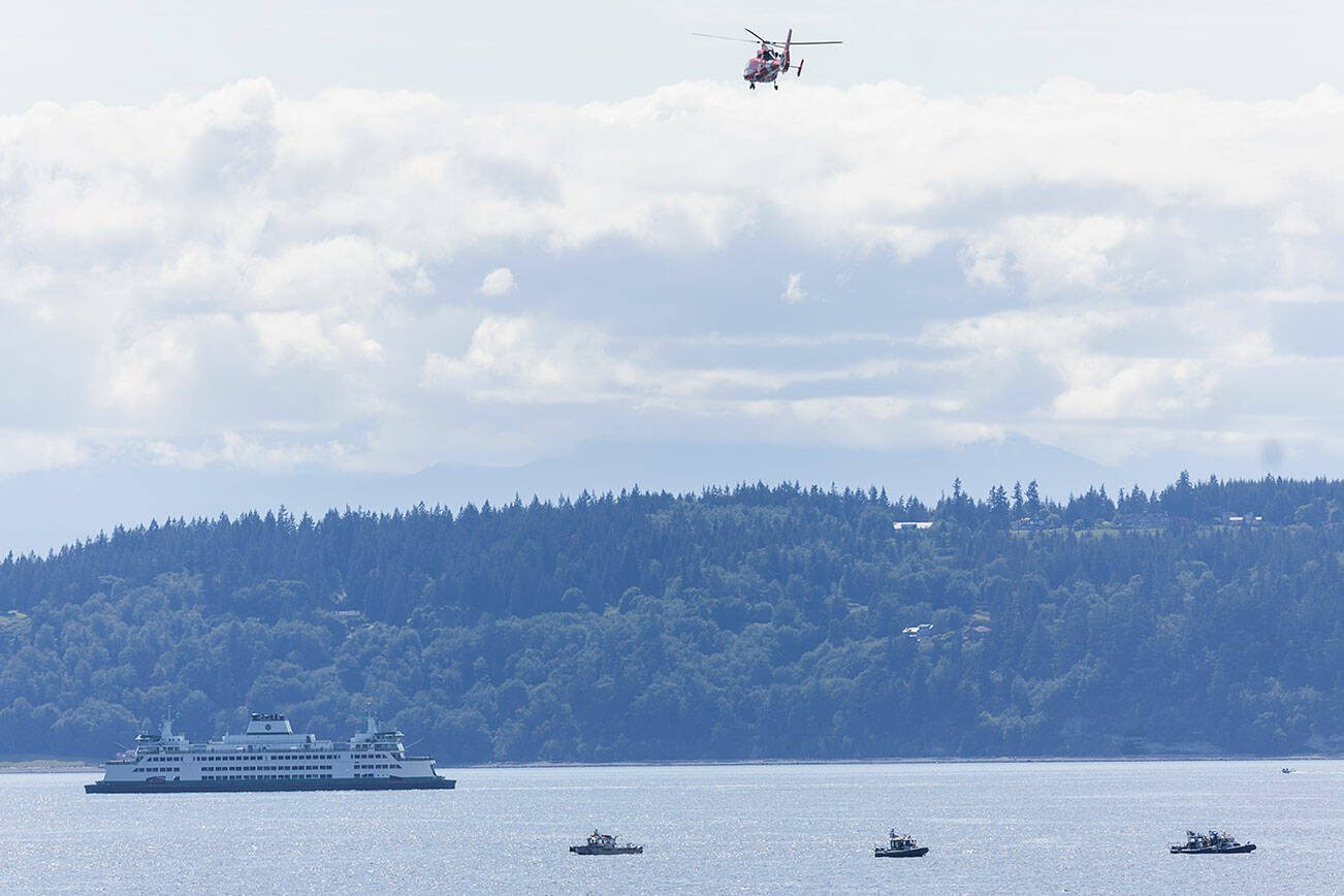 A ferry passes by as Everett Fire Department, Everett Police and the U.S. Coast Guard conduct a water rescue for a sinking boat in Possession Sound off of Howarth Park on Wednesday, May 21, 2025 in Everett, Washington. (Olivia Vanni / The Herald)