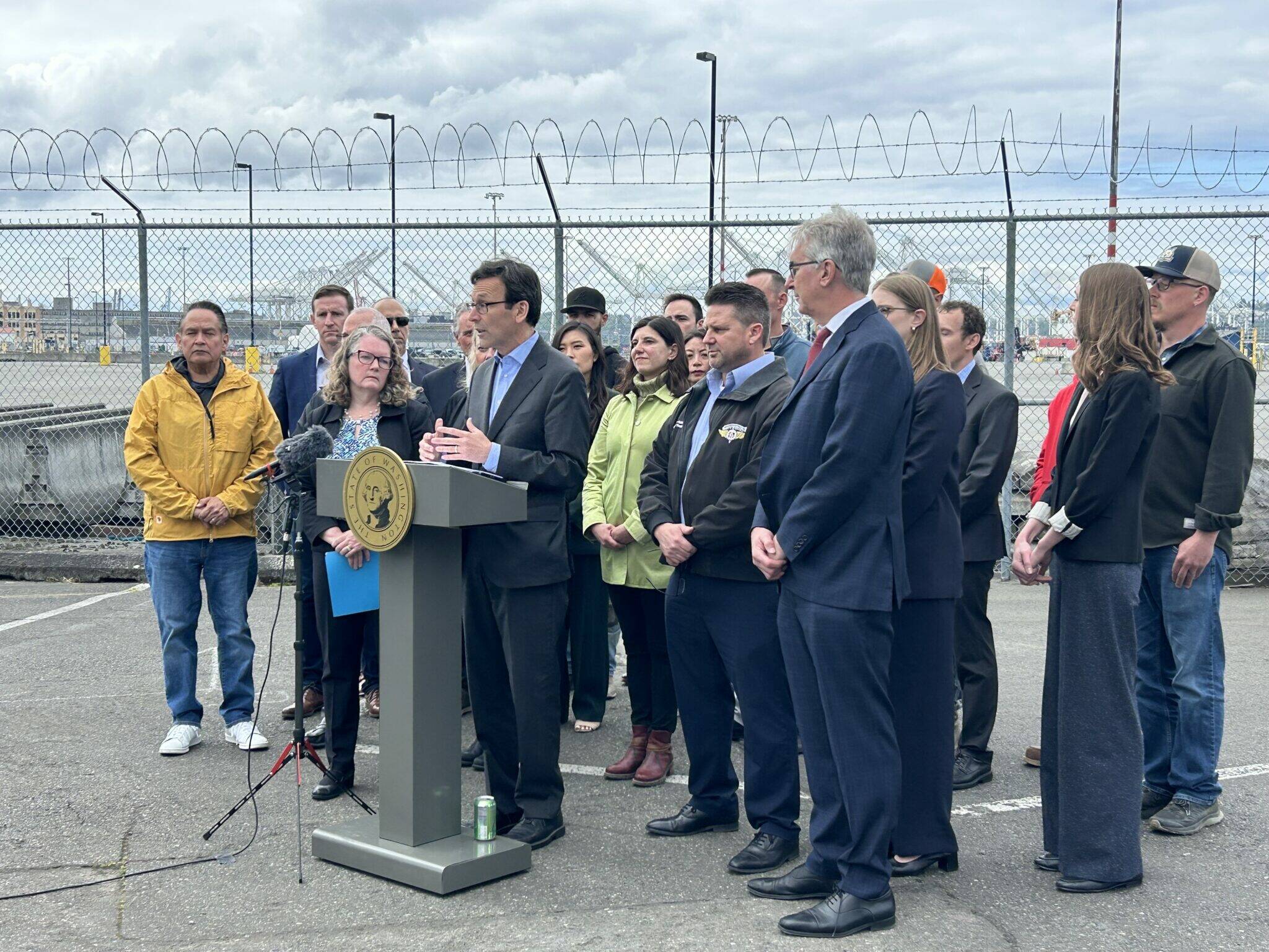 Jake Goldstein-Street / Washington State Standard
Gov. Bob Ferguson slams President Donald Trump’s tariffs in a press conference alongside union leaders, lawyers, elected officials and others at the Port of Seattle on Wednesday.