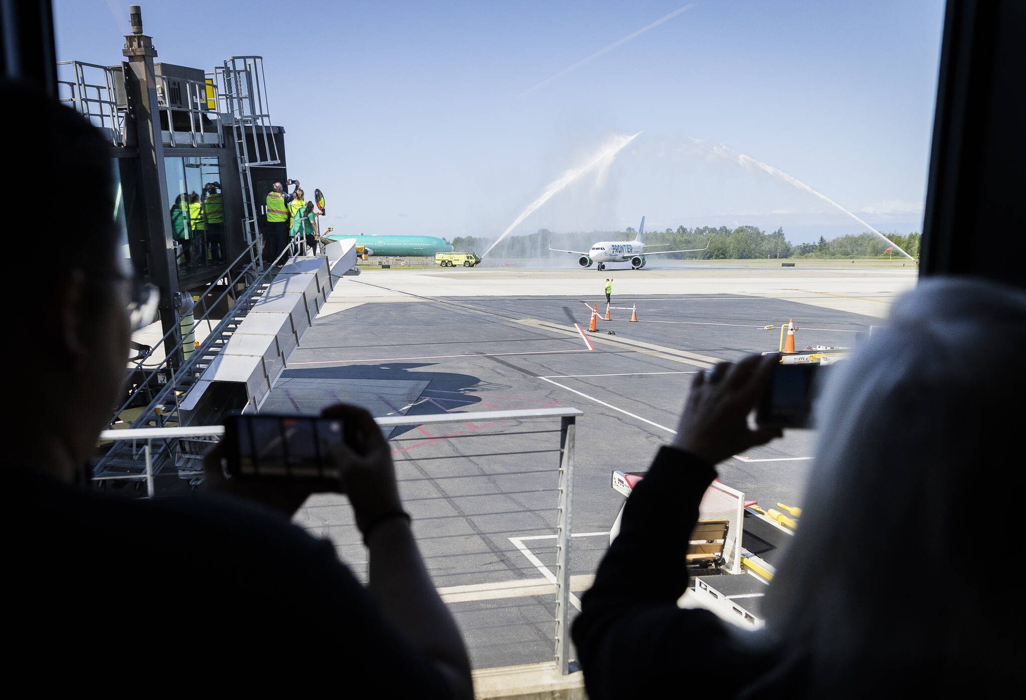 People take photos and videos as the first Frontier Arlines flight arrives at Paine Field Airport under a water cannon salute on Monday, June 2, 2025 in Everett, Washington. (Olivia Vanni / The Herald)