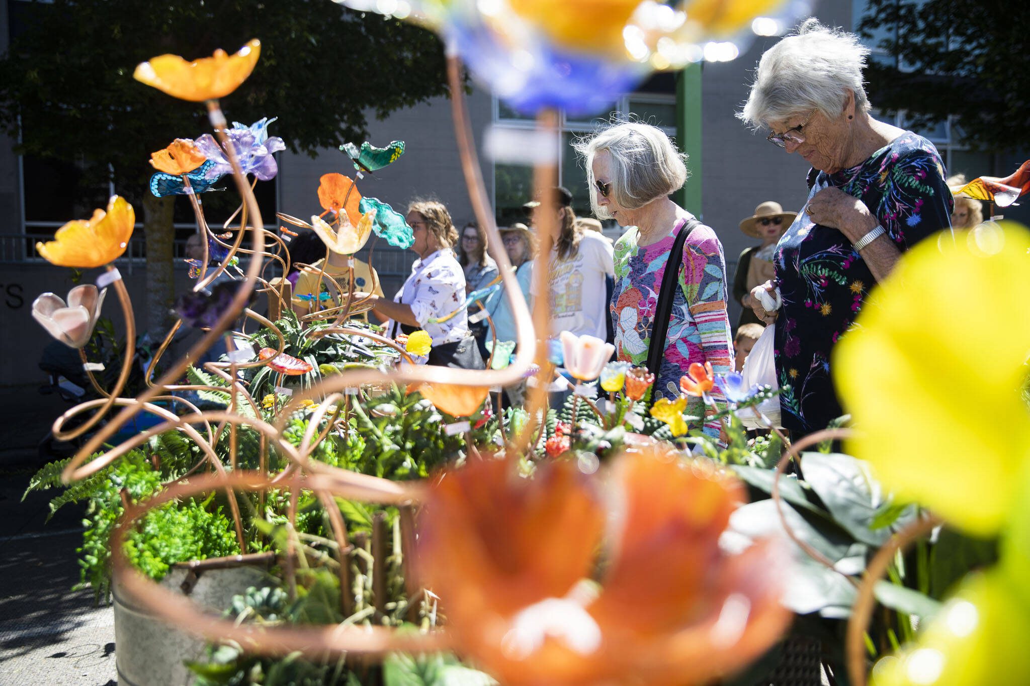 Nedra Vranish, left, and Karen Thordarson, right browse colorful glass flowers at Fuse4U during Sorticulture on Friday, June 7, 2024, in Everett, Washington. (Olivia Vanni / The Herald)