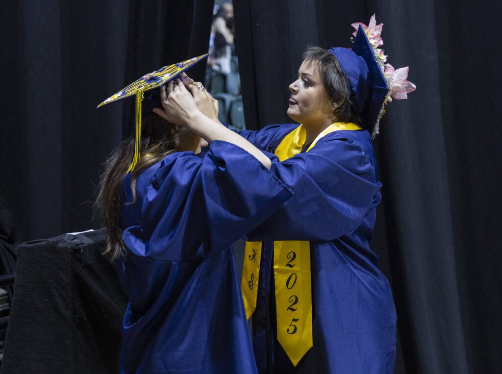 Gabriella Hurley, right, helps secure Anya Kozina’s graduation cap before the start of Mariner High School’s 2025 commencement on Friday, June 13, 2025, at Angel of the Winds Arena in Everett, Washington. (Olivia Vanni / The Herald)
