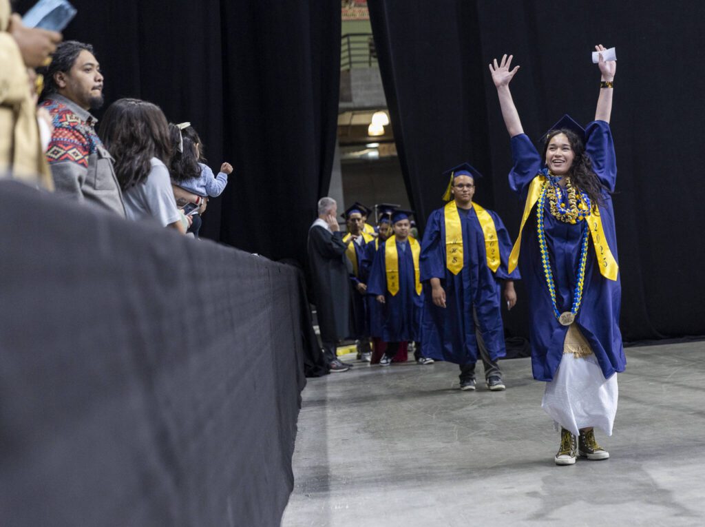 A graduate raises their arms in the air as their family cheers during Mariner High School’s 2025 commencement on Friday, June 13, 2025, at Angel of the Winds Arena in Everett, Washington. (Olivia Vanni / The Herald)
