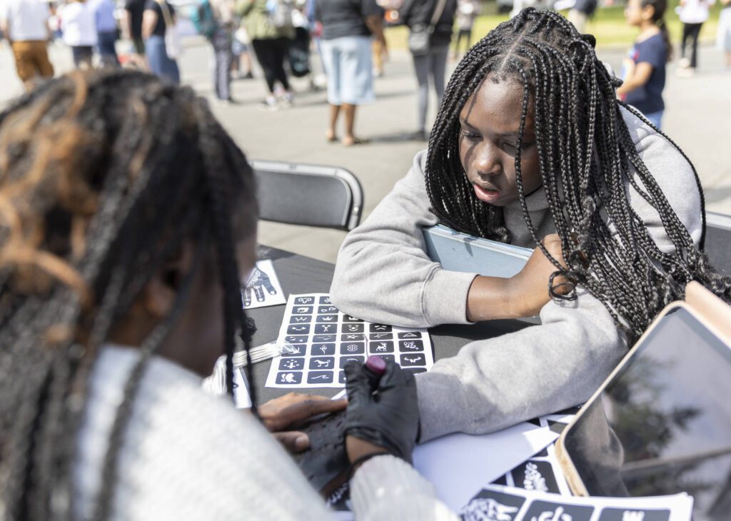 Amie Sow, right, has henna drawn on her hand by Yassin Darboe during Lynnwood Juneteenth on Thursday, June 19, 2025 in Lynnwood, Washington. (Olivia Vanni / The Herald)
