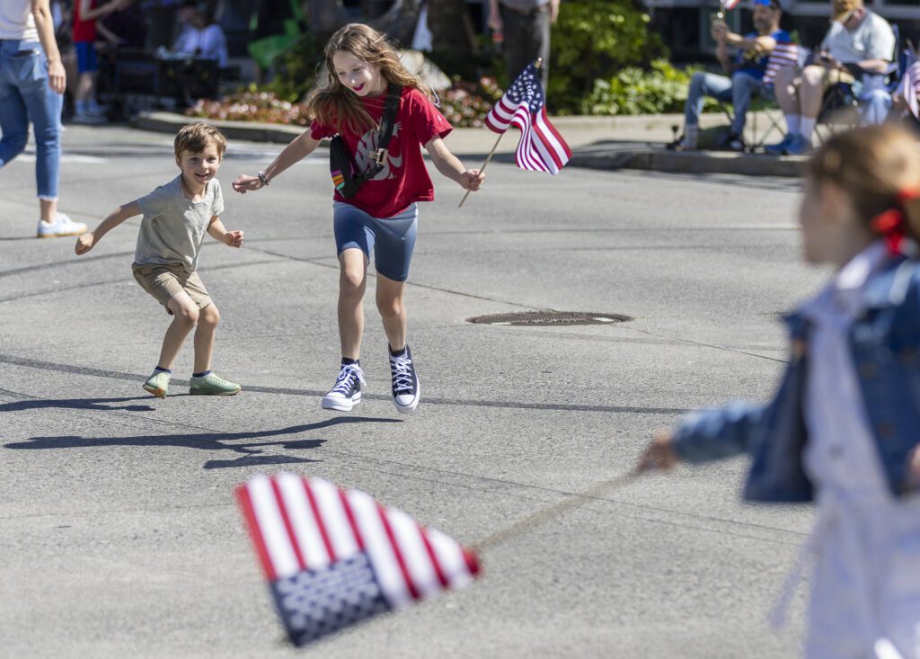 Benny Perkins, 5, and Eleanor Perkins, 8, run across Colby Avenue before the start of the Fourth of July parade on Friday, July 4, 2025 in Everett, Washington. (Olivia Vanni / The Herald)

