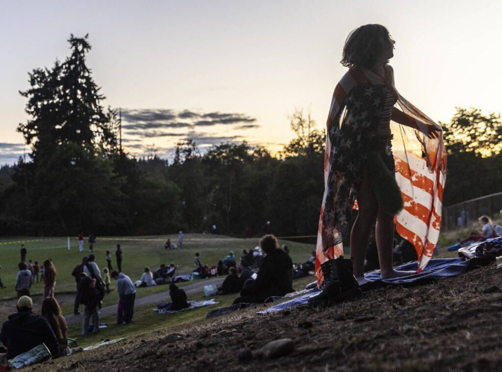 A child runs up a hill at Nile Shrine Golf Course wearing an American flag before the start of fireworks on Thursday, July 3, 2025 in Mountlake Terrace, Washington. (Olivia Vanni / The Herald)

