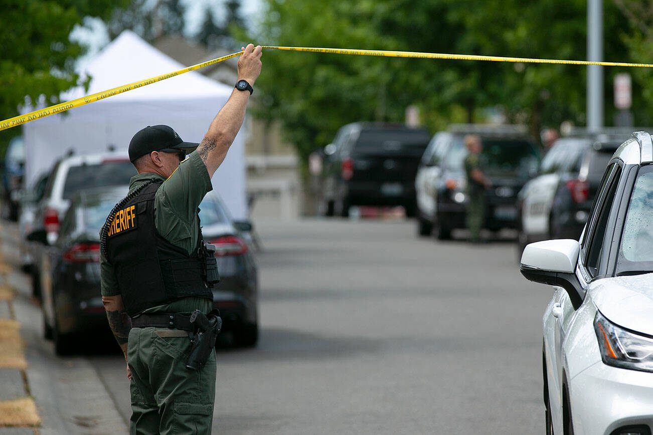 A sheriff’s deputy lets a vehicle pass police tape as law enforcement works in 2022 in Everett. (Ryan Berry / The Herald)
