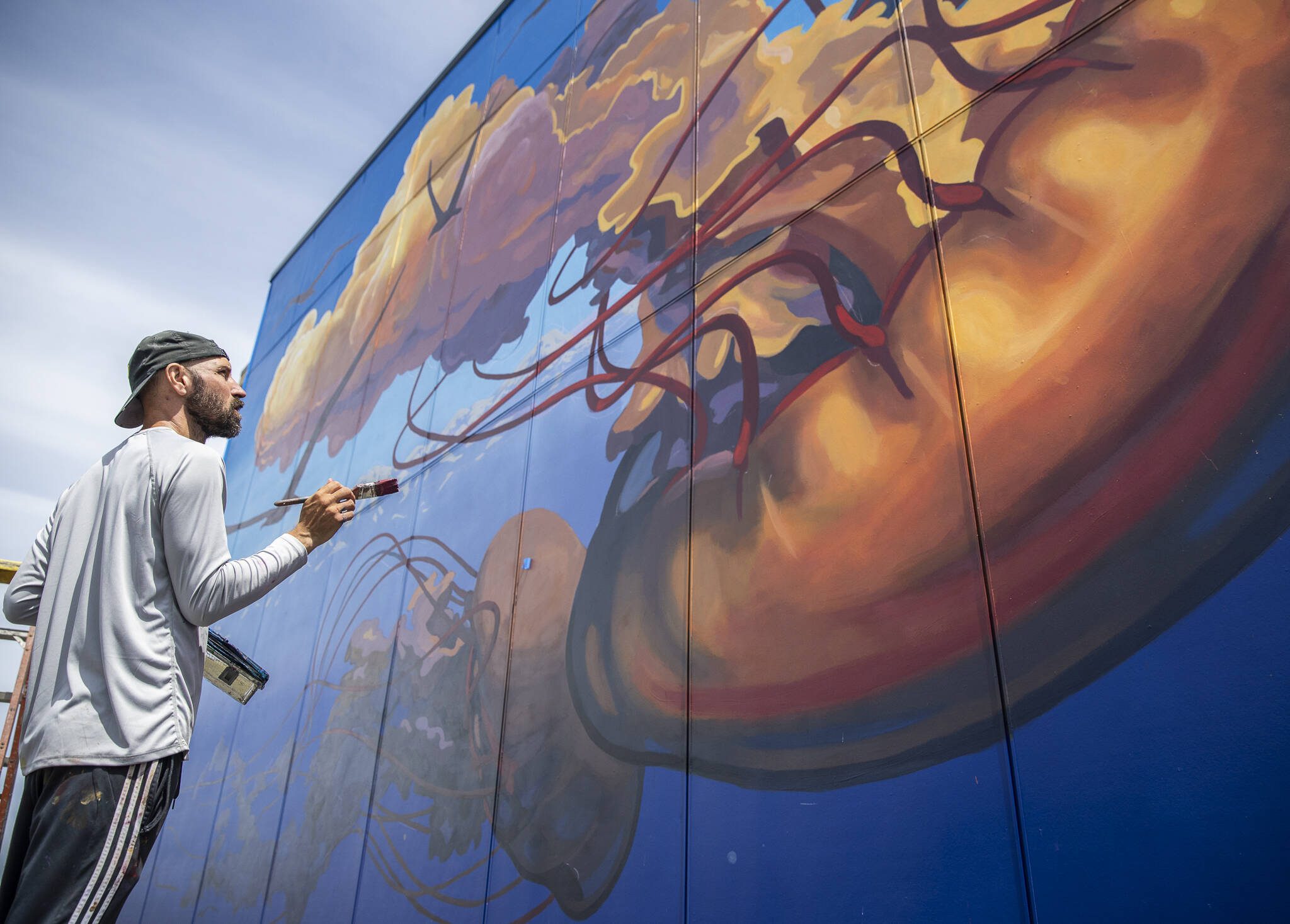 Will Schlough works on a jellyfish mural on the side of a building along Olympic Beach for Art Walk Edmonds on Thursday, June 19, 2025 in Edmonds, Washington. (Olivia Vanni / The Herald)