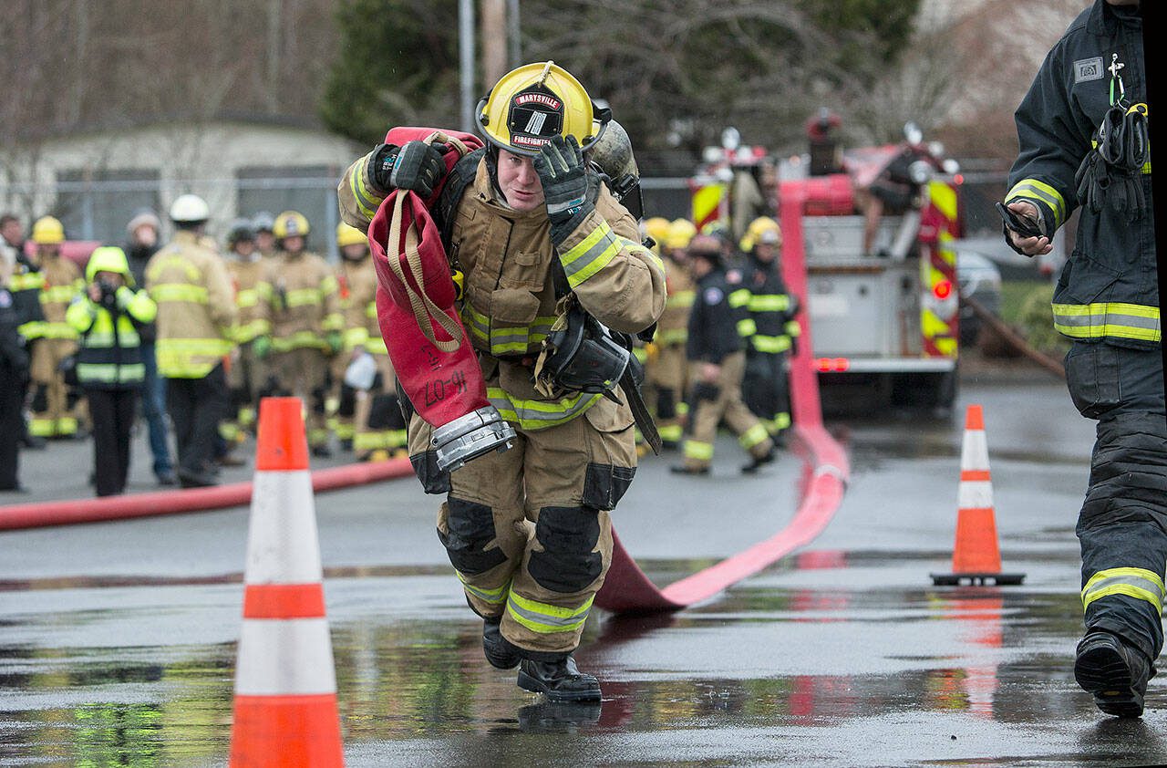 Marysville recruit Brian Donaldson, holds onto his helmet as he drags a 5-inch line 200 feet in Snohomish County’s first fire training academy run through an obstacle course at the South Snohomish Fire & Rescue training ground on Monday, March 26, 2018 in Everett, Wa. (Andy Bronson / The Herald)