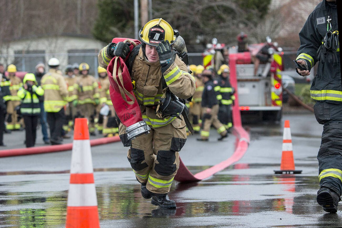 Marysville recruit Brian Donaldson, holds onto his helmet as he drags a 5-inch line 200 feet in Snohomish County’s first fire training academy run through an obstacle course at the South Snohomish Fire & Rescue training ground on Monday, March 26, 2018 in Everett, Wa. (Andy Bronson / The Herald)