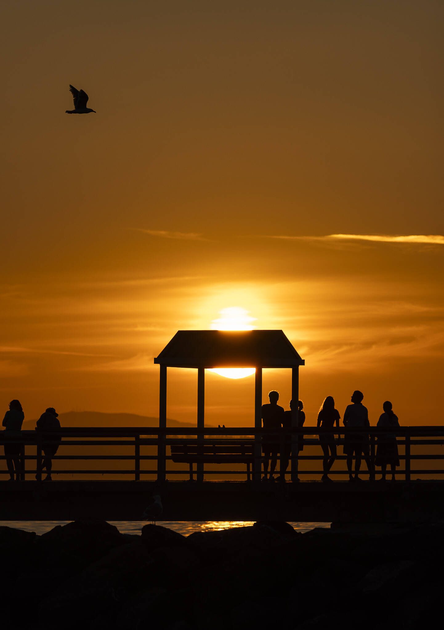The sun begins to set as people walk along the Edmonds Fishing Pier on Thursday, July 17, 2025 in Edmonds, Washington. (Olivia Vanni / The Herald)
