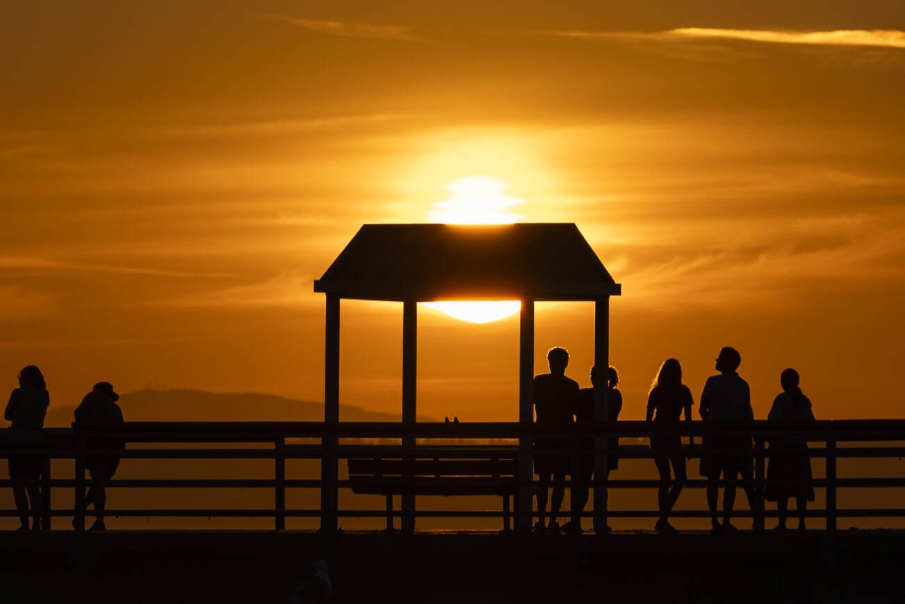 The sun begins to set as people walk along the Edmonds Fishing Pier on Thursday, July 17, 2025 in Edmonds, Washington. (Olivia Vanni / The Herald)