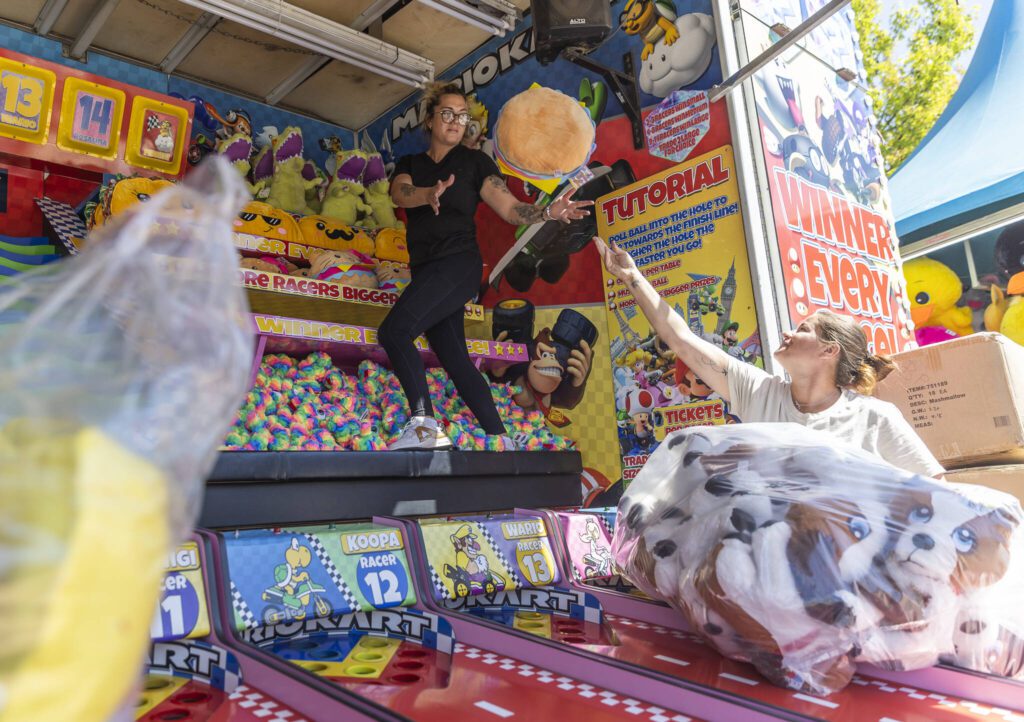 Meagan Scheeprs, left, reaches out to catch a stuffed animal thrown by Rachelle Keiser at one of their booths at the Evergreen State Fair on Wednesday, Aug. 20, 2025 in Monroe, Washington. (Olivia Vanni / The Herald)
