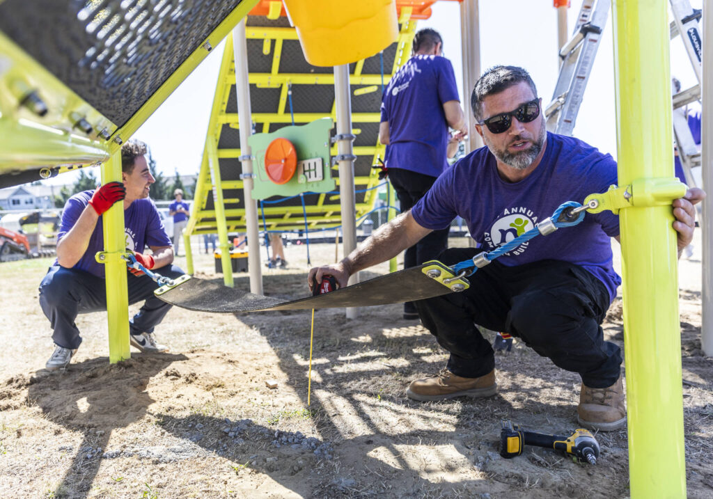 Dustin Deer, right, and Ryan Gordon, left, level a suspended seat on a play structure on Wednesday, Aug. 20, 2025 in Marysville, Washington. (Olivia Vanni / The Herald)
