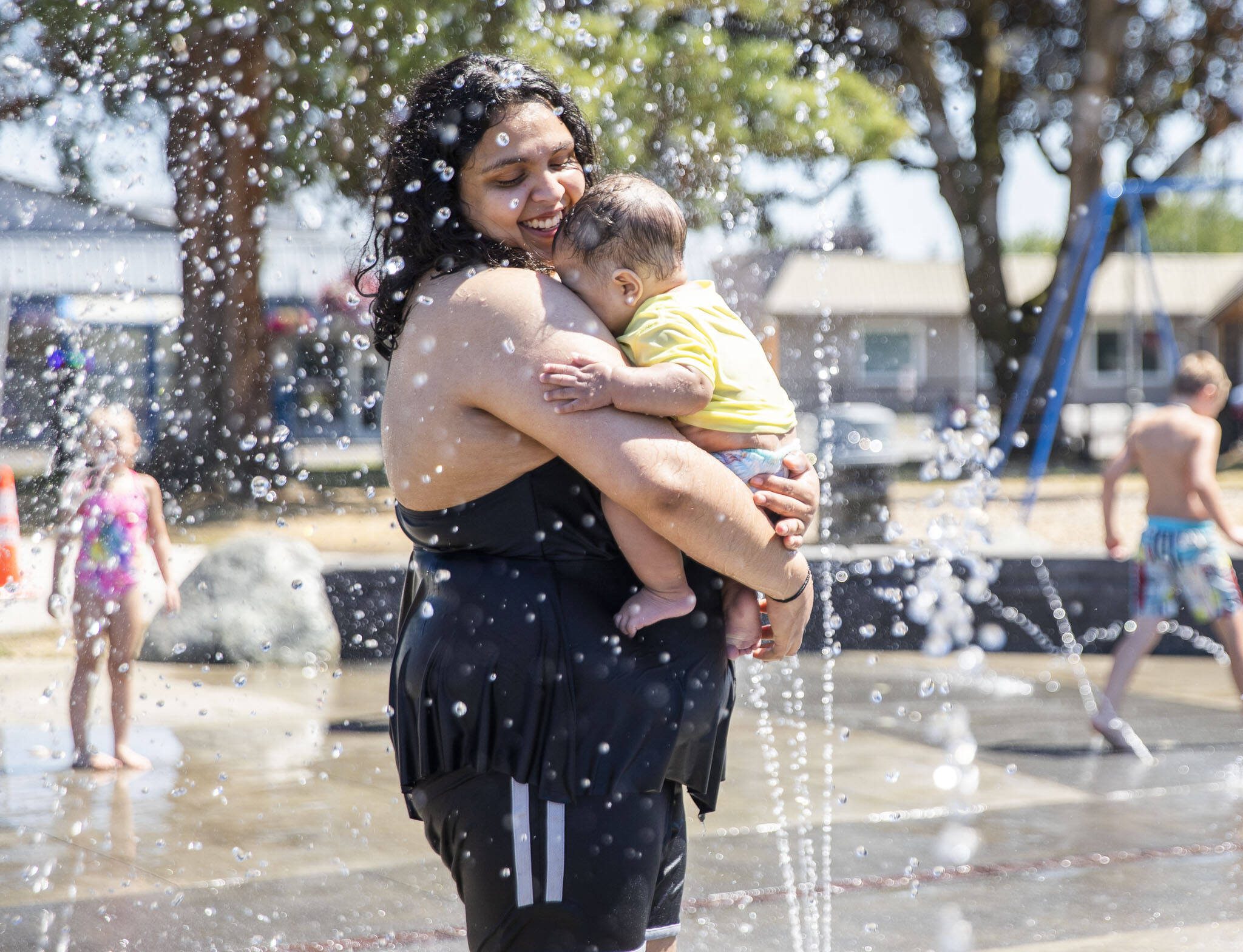 Sadie Amaya holds 7-month-old Samuel through a spray of water at Comeford Park on Tuesday, July 26, 2022 in Marysville, Washington. (Olivia Vanni / The Herald)