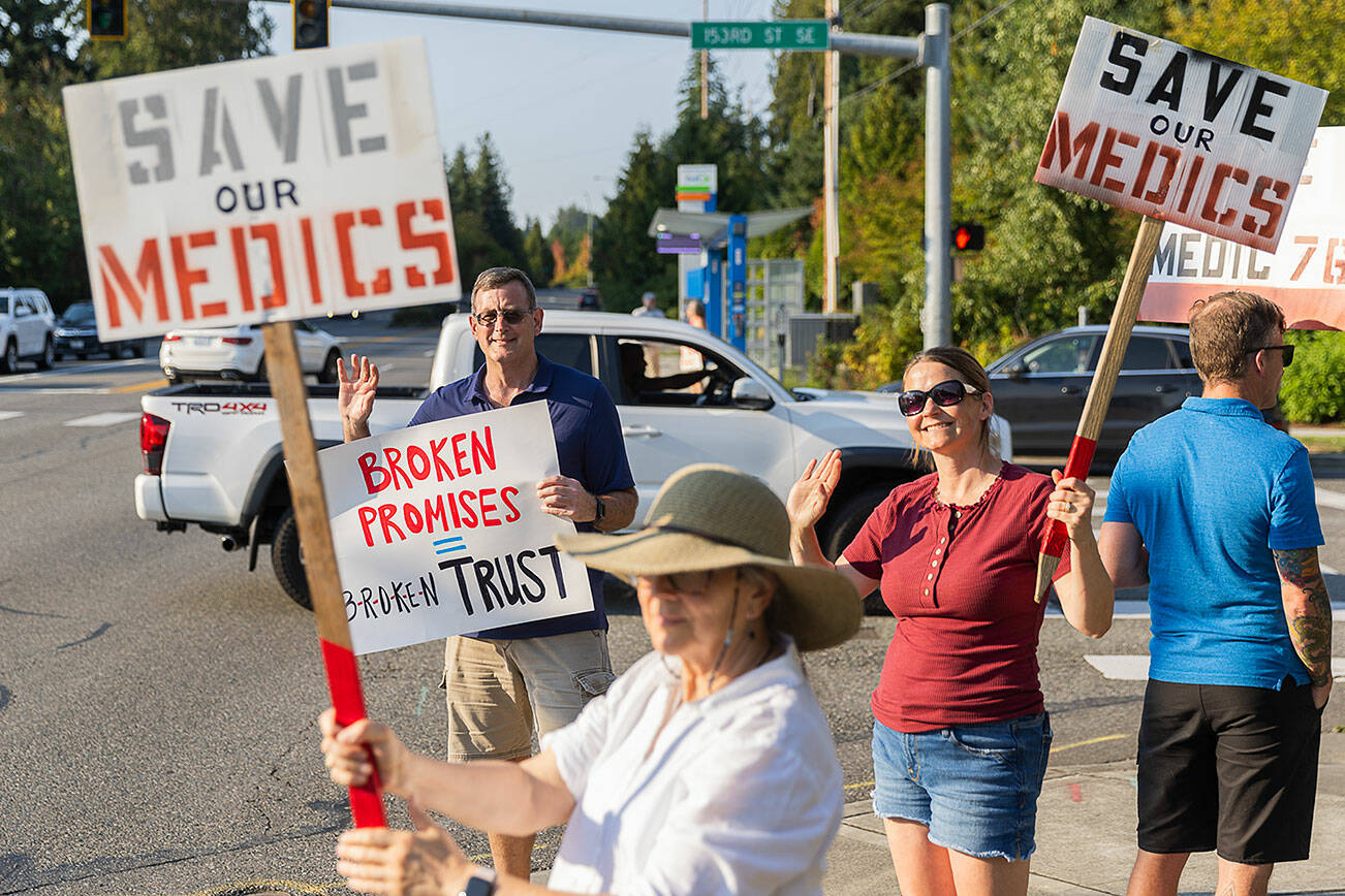 Roger Smith, left, Jan Kenndedy, center, Alison Harder, right, and other wave signs asking to restore paramedics to Station 76 on the corner of Bothell Everett Highway and 152nd Place SE on Tuesday, Aug. 26, 2025 in Mill Creek, Washington. (Olivia Vanni / The Herald)