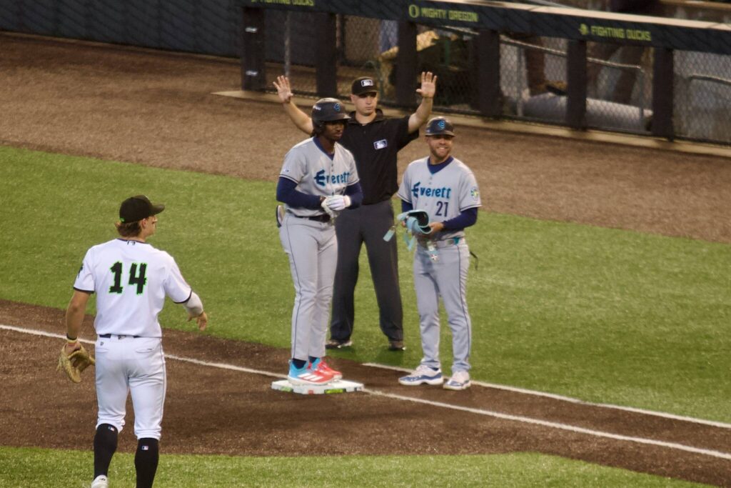 AquaSox infielder Felnin Celesten stands at first base next to bench coach Hecmart Nieves after hitting an RBI single during Everett’s 9-6 extra-innings win against Eugene in Game 1 of the Northwest League Championship Series at PK Park on Sept. 9, 2025. (Joe Pohoryles / The Herald)

