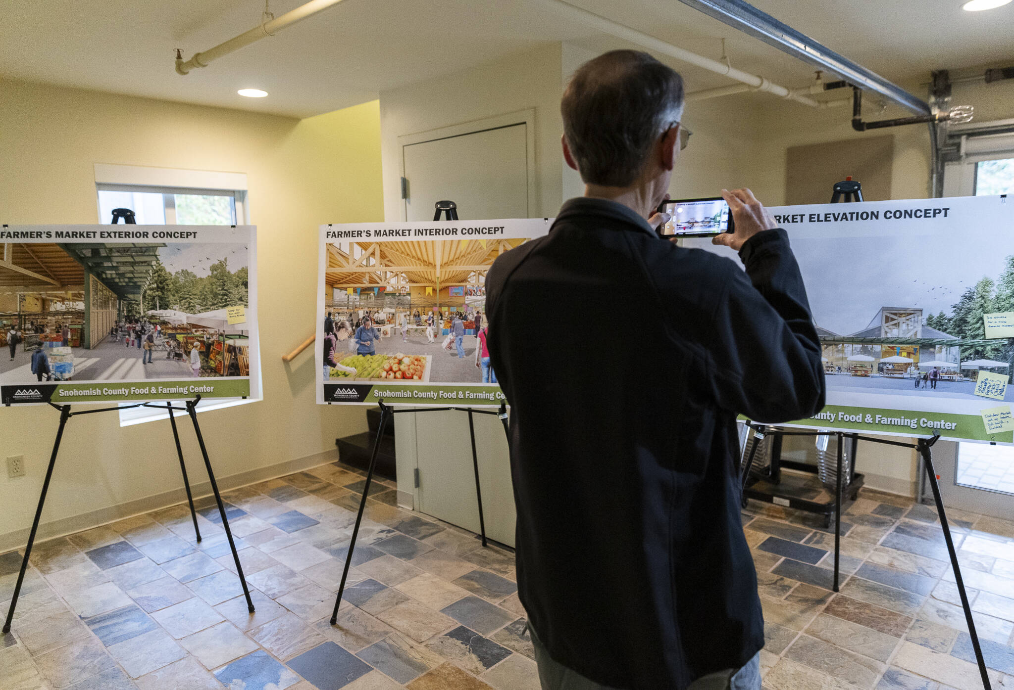 A person takes photographs of farmers market concept boards on display at the Northwest Stream Center during an informational open house on Oct. 9, 2025 in Everett, Washington. (Olivia Vanni / The Herald)