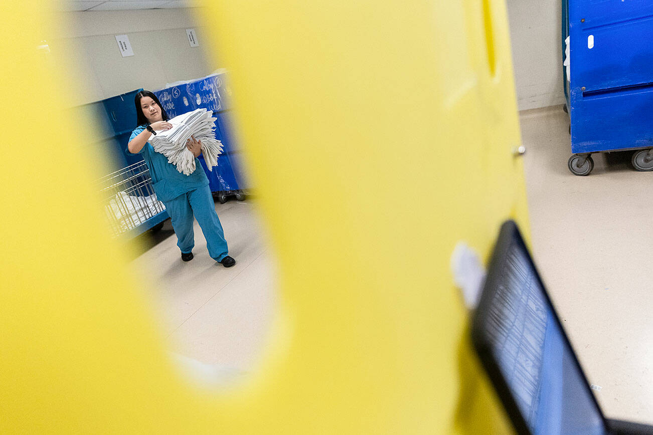 Mary Pham picks up sheets and walks them to get cart as sorts through her work orders for the day at Providence Regional Medical Center Everett on Oct. 8, 2025 in Everett, Washington. (Olivia Vanni / The Herald)
