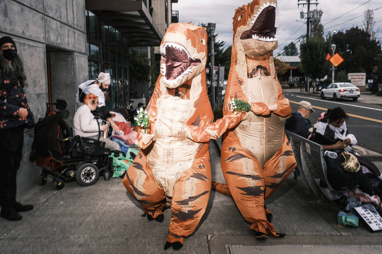 Two people in dinosaur costumes demonstrate against ICE in Portland, Ore., on Friday, Oct. 10, 2025. Images of anarchists clad in black gave the city a bad name in 2020. Now, demonstrators in Portland are poking fun at President Trump’s apocalyptic talk with colorful animal suits. (Jordan Gale/The New York Times)