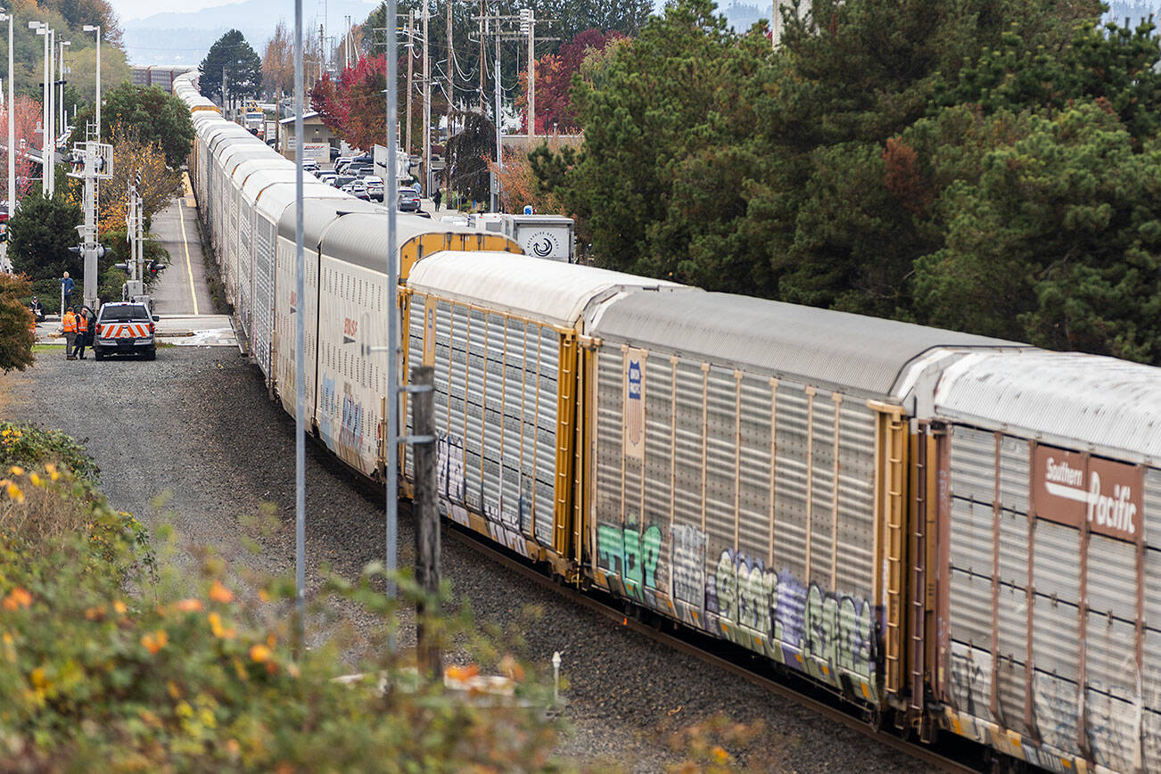 A train sits on the tracks while BNSF workers stand next to the site of a car and train collision at the intersection of Railroad Avenue and Main Street on Oct. 28, 2025 in Edmonds, Washington. (Olivia Vanni / The Herald)